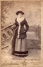 Cabinet card by the Appelquest studio in MIddletown, CT. Shows a full-length view of a woman standing by a studio set. The woman is wearing a fur-trimmed jacket. (Courtesy McIntyre-Culy collection).