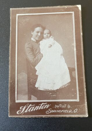 Cabinet card photo of a woman sitting with a baby on her lap.